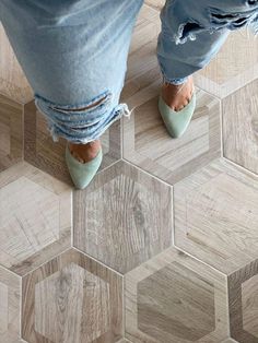 the legs of a person wearing blue jeans and green shoes standing on a wooden floor