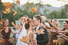 a bride and groom kissing in front of a group of people throwing leaves into the air