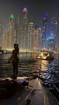 a man standing on the edge of a boat in front of a city at night