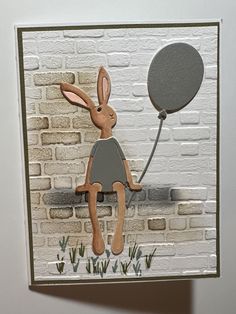 a card with an image of a rabbit sitting on a brick wall and holding a balloon