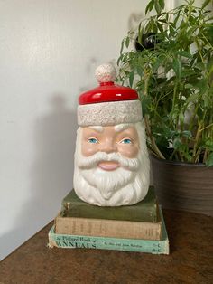 a ceramic santa claus head sitting on top of a stack of books next to a potted plant