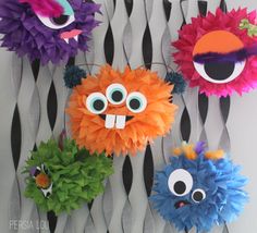 colorful paper pom poms hanging on a wall with eyes and nose decorations attached to them