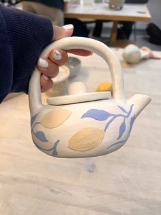 a hand holding a ceramic teapot shaped like a bird with leaves painted on it