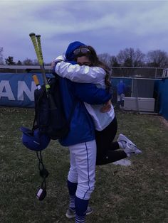 a woman in blue and white baseball uniform hugging her friend on the field with a bat