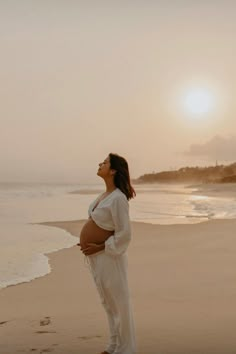 a pregnant woman standing on the beach at sunset