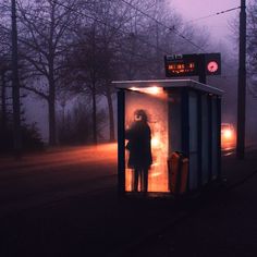 a woman is standing in a small box on the side of the road at night