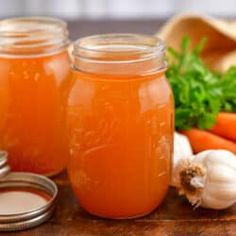 three jars filled with liquid sitting on top of a table next to carrots and garlic