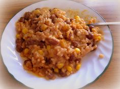 a white plate topped with rice covered in beans and corn next to a fork on top of a wooden table