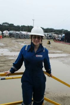 a woman in blue coveralls and white hard hat standing next to yellow pipe