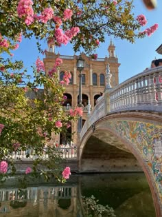 a bridge over a body of water with pink flowers in the foreground and an ornate building behind it