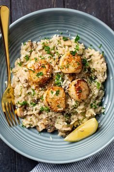 a blue plate topped with rice covered in scallops and lemon wedges next to a fork