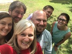 a group of people standing next to each other in the grass with one woman taking a selfie