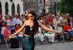 a woman in a black top and green skirt is dancing on the street with an audience