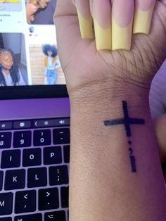 a person with a cross tattoo on their wrist next to a laptop computer and keyboard