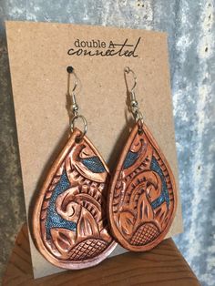 "Our carved leather earrings are one of our original designs and a classic. Each earring is hand-carved and then hand tooled. A blue metallic background hand-painted on finishes the piece with extra pop. These are our largest teardrop earrings and a favorite because of the classic carved leather design and tooling. As with all our leather earrings they are incredibly lightweight. These come in two color options: Antique Brown and Saddle Tan (pictured). The blue background will be the same. *NEW* Artisan Hand-tooled Teardrop Earrings, Unique Hand-tooled Teardrop Earrings, Artisan Hand Tooled Drop Earrings, Artisan Hand-tooled Drop Earrings, Blue Bohemian Hand-tooled Earrings, Artisan Blue Leather Jewelry, Blue Metallic Background, Makerspace Projects, Metallic Background