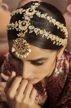 a woman wearing a gold headpiece with pearls and beads on her hair is looking down