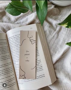 an open book sitting on top of a bed next to a green leafy plant