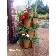 a tall planter filled with lots of flowers next to a brick wall in front of a house