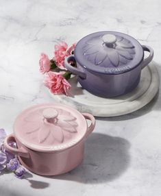 two pink and purple pots sitting on top of a white counter next to some flowers