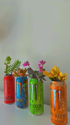 three cans with plants and flowers in them on a table next to a vase filled with succulents