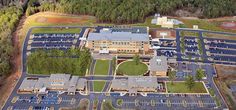 an aerial view of a large building with lots of parking spaces and trees in the background