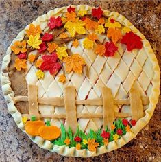 a pie decorated with leaves and flowers on top of a granite countertop next to a wooden fence