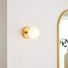 a white vase sitting next to a gold framed mirror on the side of a wall