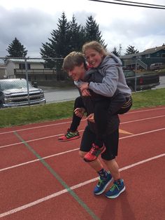 a man carrying a woman on his back while standing on a running track in front of a fence