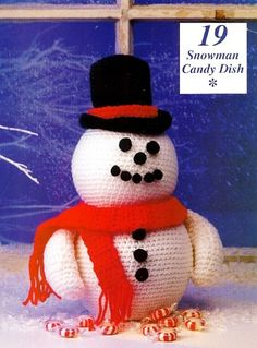 a knitted snowman wearing a red scarf and black top hat, standing in the snow