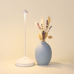 a blue vase with dried flowers in it next to a white light on a table