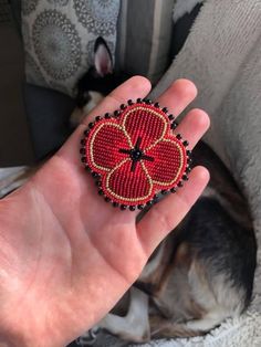 a hand holding a red beaded brooch on it's left side with a dog sleeping in the background