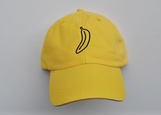 The best banana hat there is! Our official Banana Soup logo stitched onto a dad hat. Available in Yellow. Our recipe for the best hat: -The official Banana Soup logo embroidered design centered on the front of the hat -100% cotton material  -Adjustable, tuck-away leather back strap with antique brass closure. Strap includes the Adams logo -One size fits most (fit intended for adults) -A pre-curved bill -Exclusive cool-crown mesh for added comfort -Slightly faded look *As each hat is stitched sep Soup Logo, Banana Hat, Banana Soup, The Adams, Embroidered Hat, Embroidered Hats, Dad Hat, Embroidered Design, Back Strap