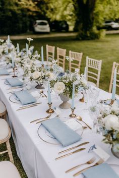 a long table with blue napkins and white flowers on it is set for an outdoor dinner