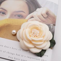 a brooch with a flower on it sitting on top of an open book next to a woman's face