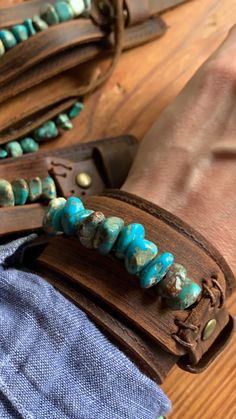 a wooden bracelet with turquoise beads on it and a person's hand next to it