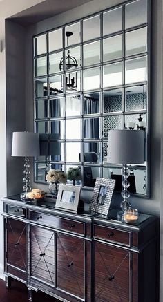 a large mirror is on the wall above a dresser with two lamps and a lamp