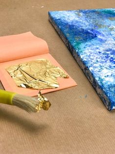 a paintbrush sitting on top of a piece of paper next to a gold leaf