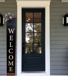 a welcome sign is on the front door of a gray house with black shutters