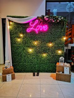 a love sign is on display in front of a wall covered with artificial plants and lights