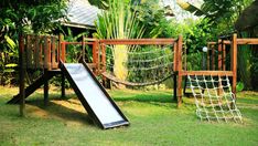 a wooden play set with a slide and hammock in the grass next to trees