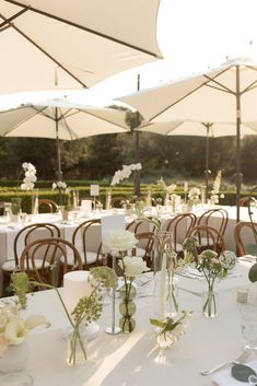 the tables are set with white flowers and umbrellas for an outdoor wedding reception at sunset