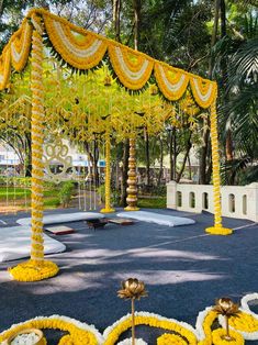 an outdoor area decorated with yellow and white flowers, garlands and decorations on the ground