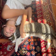 a woman laying on top of a rug next to a gray and white cat with her eyes closed