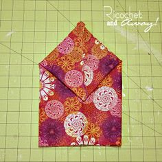 an origami style envelope made with red and pink fabric on a green cutting board