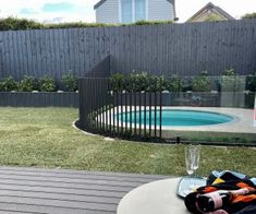 an empty glass on a table in front of a swimming pool and fenced yard