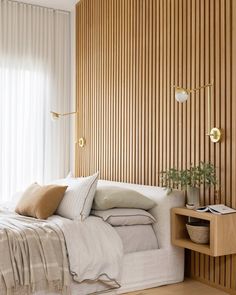 a white bed sitting in a bedroom next to a wooden headboard and wall with vertical blinds