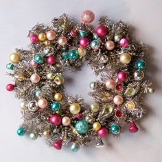 a christmas wreath made out of tinsel with ornaments around it on a white surface