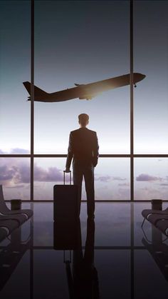 a man standing in front of an airport window with a suitcase and plane flying overhead