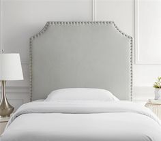 an upholstered bed with white linens and silver accents, in a bedroom