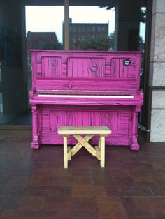 a pink piano sitting on top of a wooden bench in front of a glass window